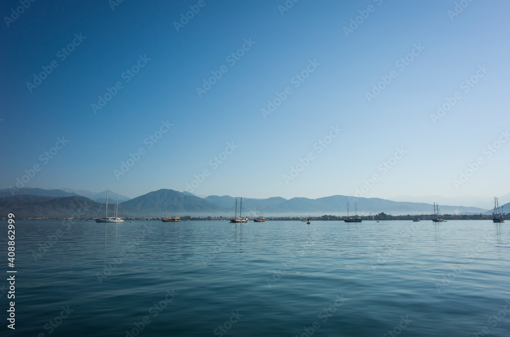 Seascape with calm blue water, yachts and mountains on horizon in Fethiye bay, Turkey. Sunny day perfect blue sky