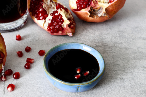 Pomegranate molasses in small bowl. Pomegranate sweet and sour syrup with pomegranate fruit and seeds on gray background. photo