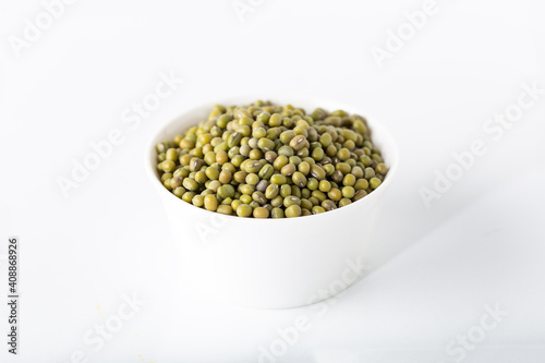 Bowl of uncooked mung beans on white background.