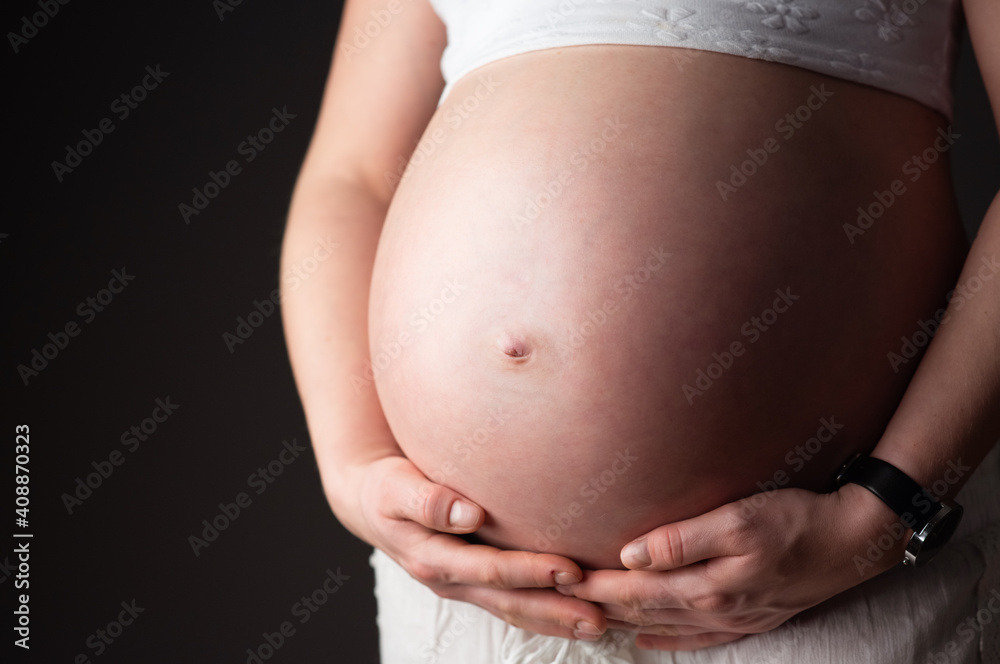 Belly of a pregnant woman from side. Dark background, copy space Belly of a pregnant woman from side. Dark background, copy space