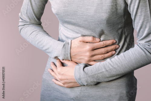 Young female suffering from stomach - pain include menstruation pain, gastritis, stomach ulcer, food poisoning, diarrhea or IBS. Close up woman holding belly, feeling discomfort.