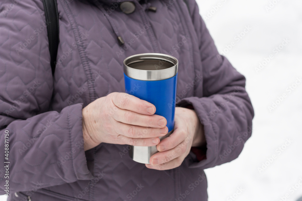 a woman holds a blue thermocup with hot tea in her hands a woman holds a blue thermocup with hot tea in her hands