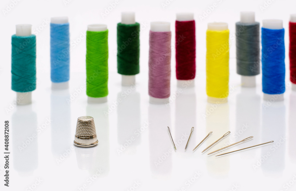 A thimble and a few sewing needles on a white glass background. In the background there are spools of thread. Selective focusing on the thimble. A thimble and a few sewing needles on a white glass background. In the background there are spools of thread. Selective focusing on the thimble.