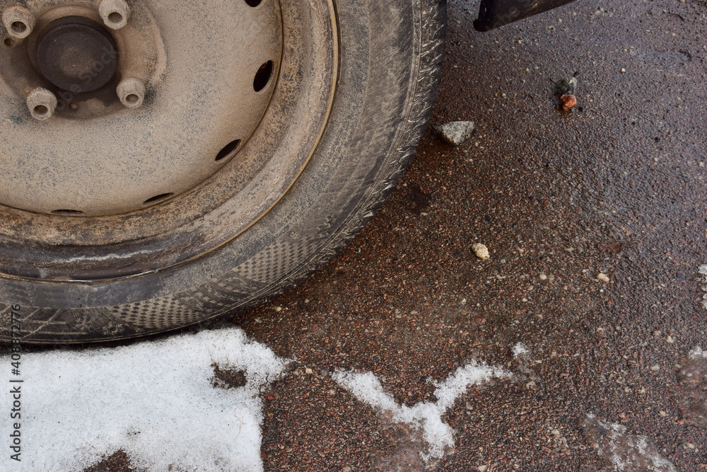 Dirty wheel of a passenger car on the snow-covered asphalt close-up