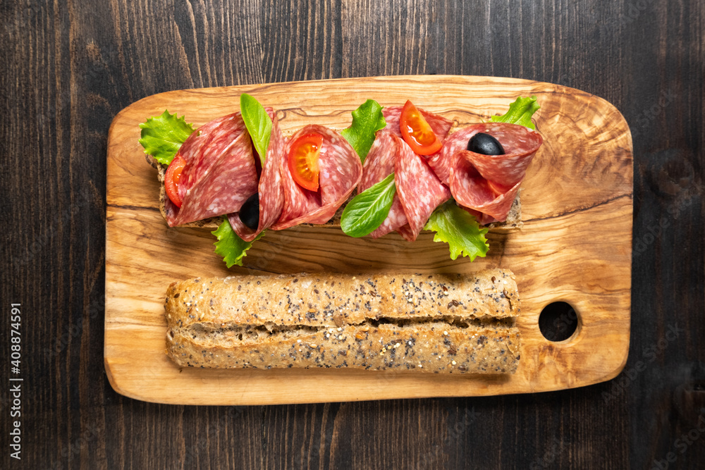 Salami sandwich with multigrain bread baguette with green lettuce and tomato. Takeaway Takeout food. Submarine sandwich top view. Healthy lunch dinner Salami sandwich with multigrain bread baguette with green lettuce and tomato. Takeaway Takeout food. Submarine sandwich top view. Healthy lunch dinner