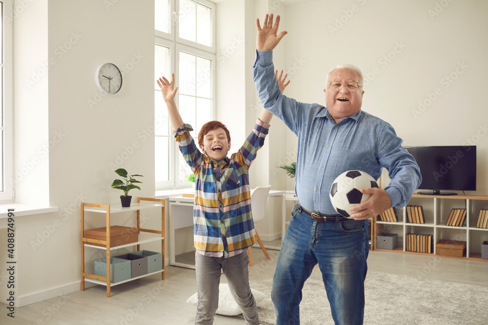 Excited grandfather and teen grandson enjoying free time, playing sports games together, having fun and celebrating victory of favorite soccer team. Happy childhood and active senior lifestyle concept - obrazy, fototapety, plakaty 