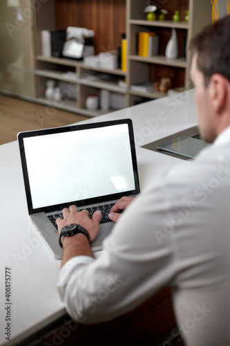 Back view of handsome mature man in casual clothes using a laptop while sitting at the table in office