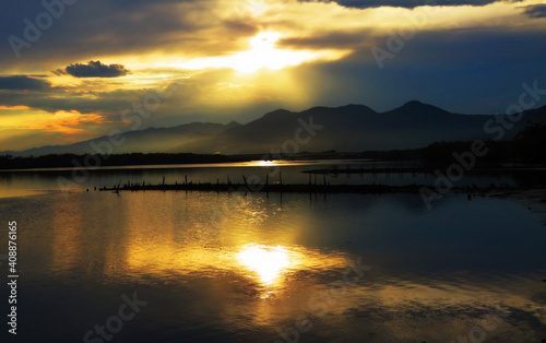 Orange sunset with rays over the mountains and reflections in the lake