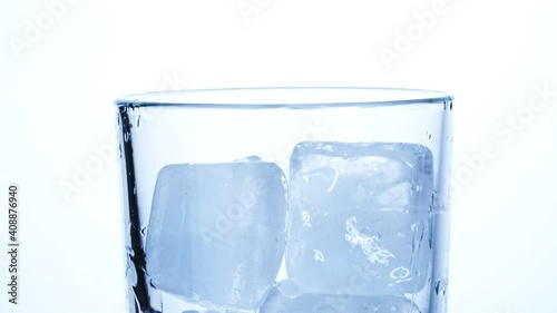 Close-up of ice cubes falling into an empty transparent glass on a white background. Slow motion.