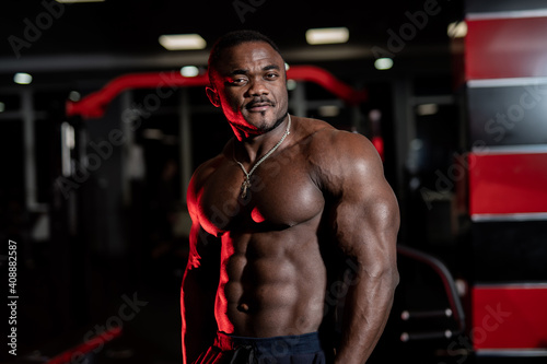 Shirtless strong bodybuilder with perfect abs poses to the camera. Modern gym background. African american athlete.