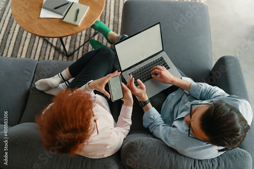 Top view of family couple resting on comfy couch having fun using laptop and phone