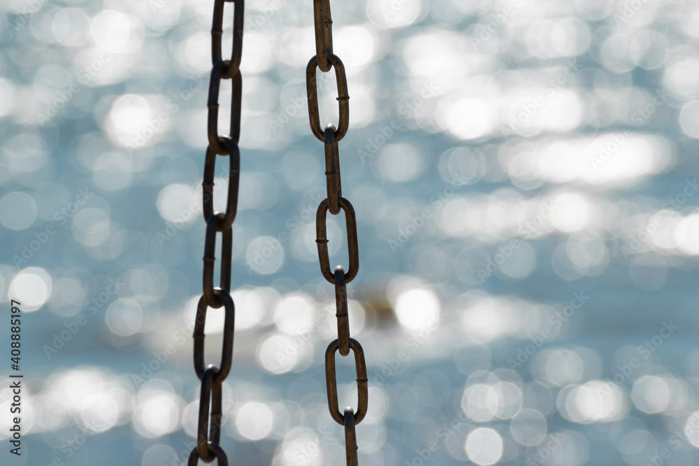 Metal chain from a swing isolated on sparkle water. Beautiful defocused sea background Metal chain from a swing isolated on sparkle water. Beautiful defocused sea background