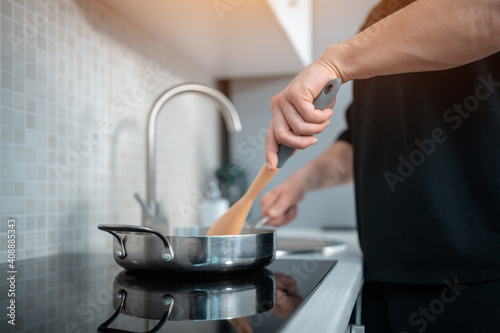 closeup of man hand cooking in pan with wooden spoon at modern home kitchen