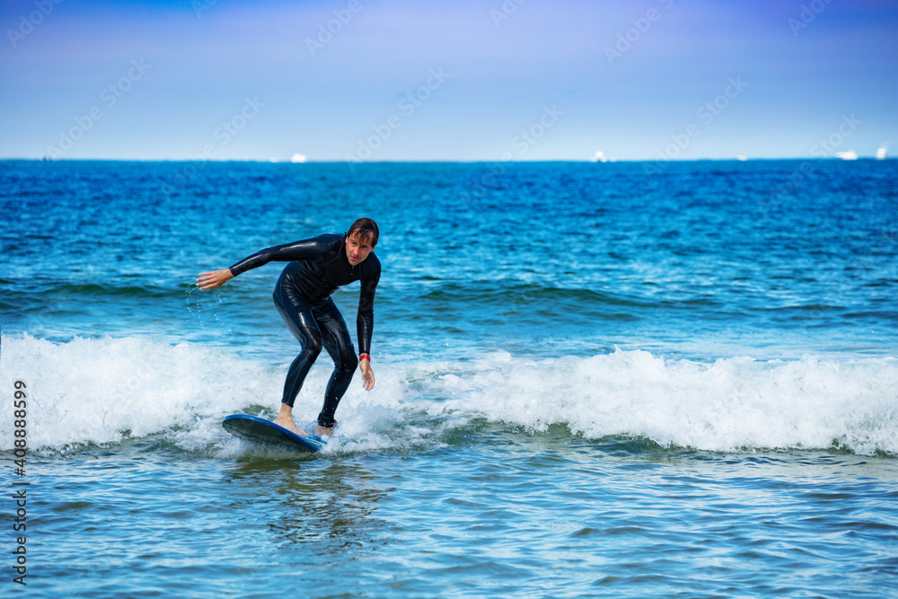 Man learns to surf on the surfboard getting used to standing on the board on small waves
