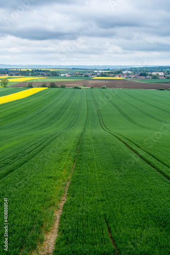 zielone i żółte pola uprawne na pierwszym planie, zabudowania w oddali i szaro-niebieskie niebo ponad nimi © Andrzej Michaluk