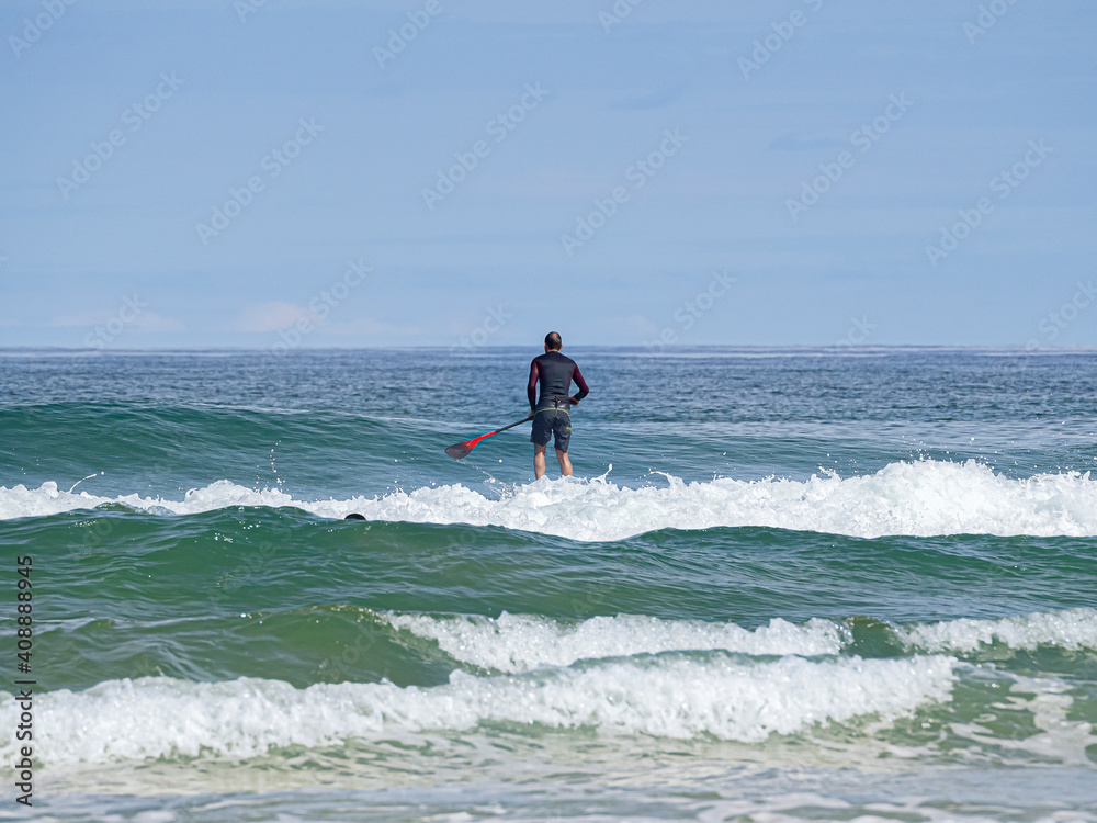 Padelsurfista con su tabla y su pala navegando sobre las olas del mar Cantábrico en la Playa del Rosal en Cantabria, verano de 2020. Padelsurfista con su tabla y su pala navegando sobre las olas del mar Cantábrico en la Playa del Rosal en Cantabria, verano de 2020.