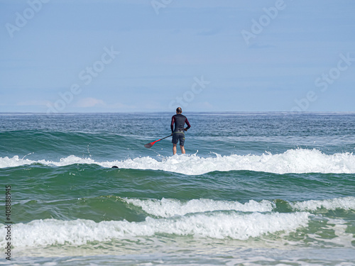 Padelsurfista con su tabla y su pala navegando sobre las olas del  mar Cantábrico en la Playa del Rosal en Cantabria, verano de 2020.