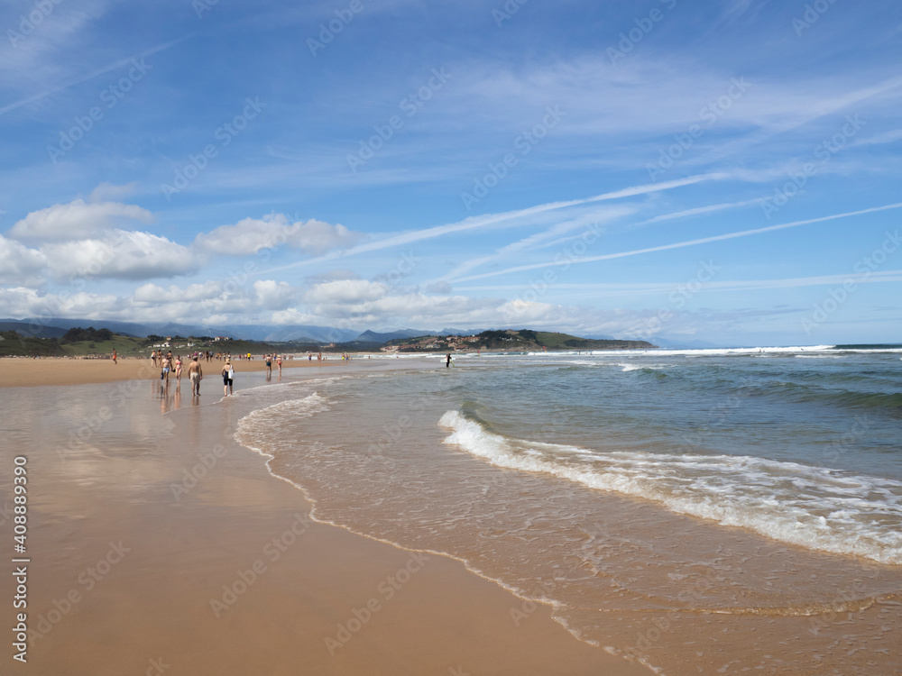 Hermosas vistas de costa con el agua llegando a la orilla y las vistas de montañas y nubes al fondo en la Playa del Rosal en Cantabria, verano de 2020