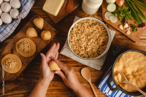 Hands of woman preparing brazilian croquette (coxinha de frango) on a wooden kitchen table - Top view photo