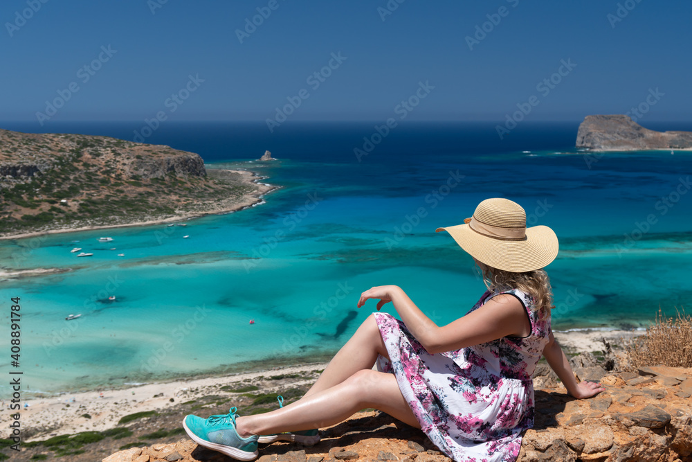 Panoramic view of Balos Lagoon, with magical turquoise waters, lagoons, tropical beaches of pure white, pink sand and Gramvousa island on Crete, Greece. Girl with blond curly hair and a cap posing