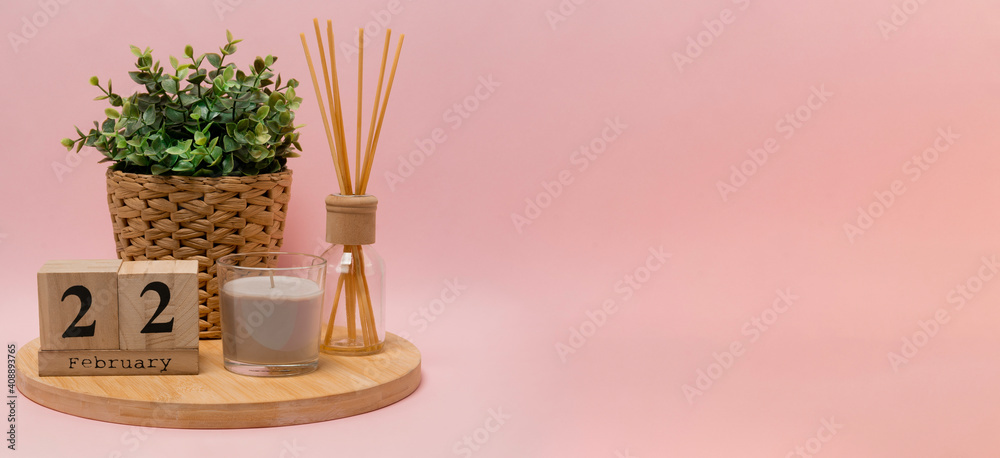 calendar. 22 february composition from a wooden calendar, a flower in a wicker pot, a gray candle in a glass candlestick and an aroma diffuser on a light pink background banner business calendar. 22 february composition from a wooden calendar, a flower in a wicker pot, a gray candle in a glass candlestick and an aroma diffuser on a light pink background banner business