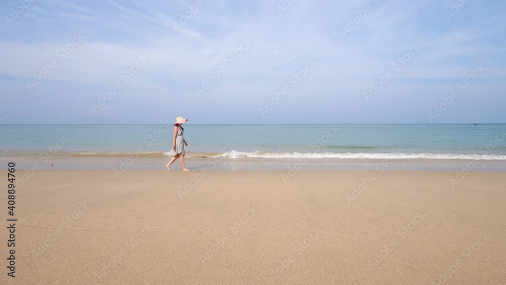 Beautiful beach, tourist woman walk along water, enjoy fresh breeze from sea. Small waves break and wash on sand, no other people around. Ko Lanta beach at Thailand Beautiful beach, tourist woman walk along water, enjoy fresh breeze from sea. Small waves break and wash on sand, no other people around. Ko Lanta beach at Thailand