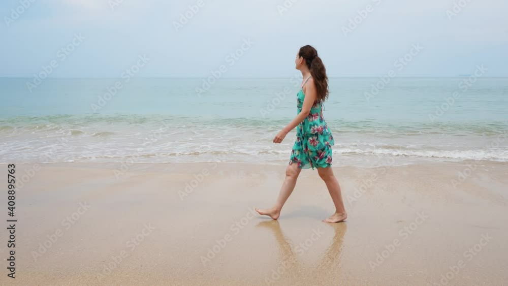 Woman stroll along beach, small waves curl and water wash flat sand. Tourist lady go along empty shore, enjoy warm and cloudy weather, typical spring day in Thailand Woman stroll along beach, small waves curl and water wash flat sand. Tourist lady go along empty shore, enjoy warm and cloudy weather, typical spring day in Thailand
