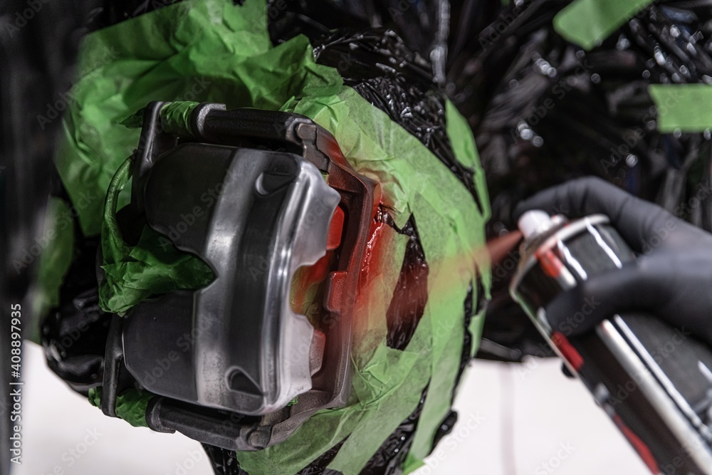 Man mechanic painting brake calipers with red paint