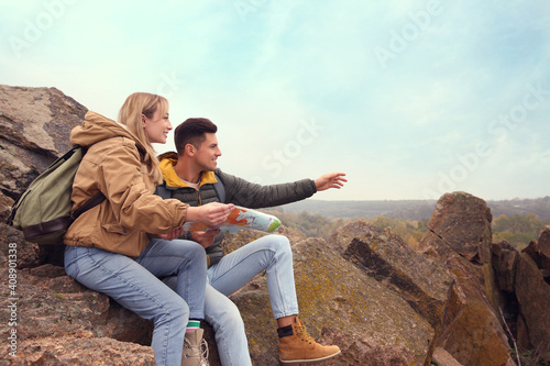 Couple of travelers with backpacks and map sitting on steep cliff. Autumn vacation