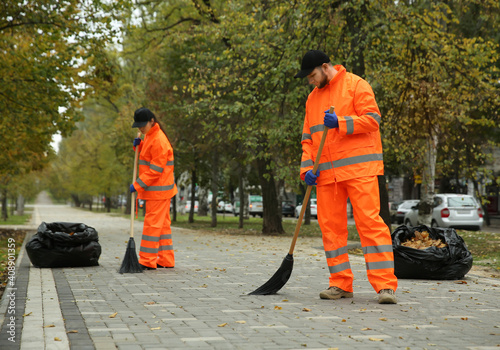 Foto Street cleaners sweeping fallen leaves outdoors on autumn day