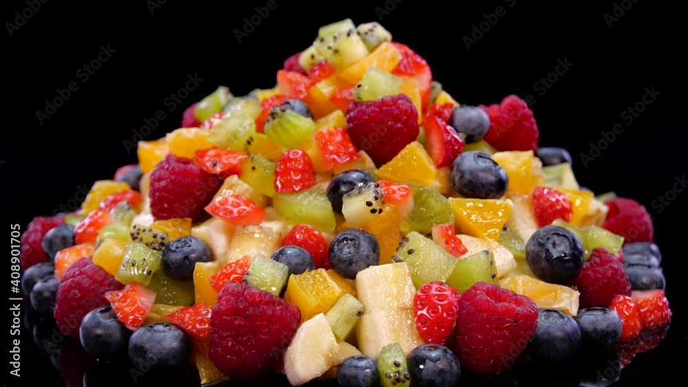 Colorful fruit salad rotating on a black background in 4K. Close up of fresh and tasty salad with orange, apple, berries, pomegranate, kiwi, ananas, raspberries, blueberries and strawberries Colorful fruit salad rotating on a black background in 4K. Close up of fresh and tasty salad with orange, apple, berries, pomegranate, kiwi, ananas, raspberries, blueberries and strawberries