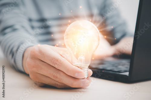 businessman hand holding light bulb and working with computer on the desk, saving energy and money,The idea of ​​inspiration from online technology.innovation idea, Intellectual imagination concept. photo