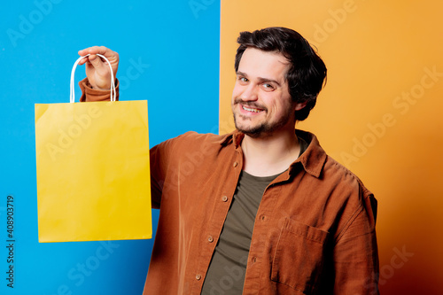 Guy in shirt hold shopping bag on yellow and blue background