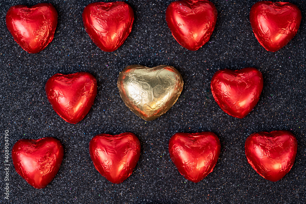 heart shaped chocolates in red foil on black background with sparkles heart shaped chocolates in red foil on black background with sparkles