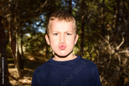 Young boy in a dark forest putting up duck faces to spoil a preadolescent photo