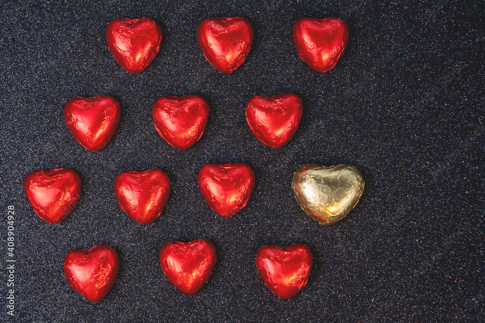 heart shaped chocolates in red foil on black background with sparkles heart shaped chocolates in red foil on black background with sparkles