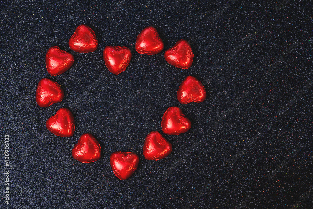 heart shaped chocolates in red foil on black background with sparkles