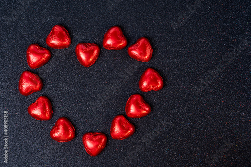 heart shaped chocolates in red foil on black background with sparkles