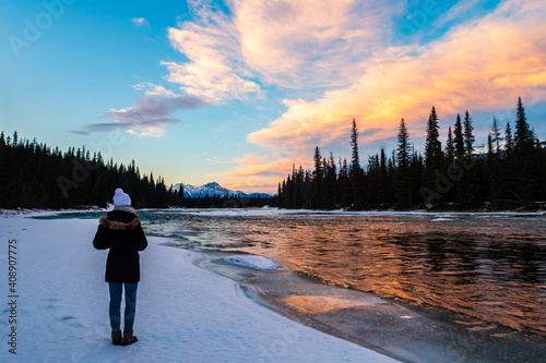 Fotografie Back view of a woman admiring a colorful sunset sky reflecting in the Athabasca