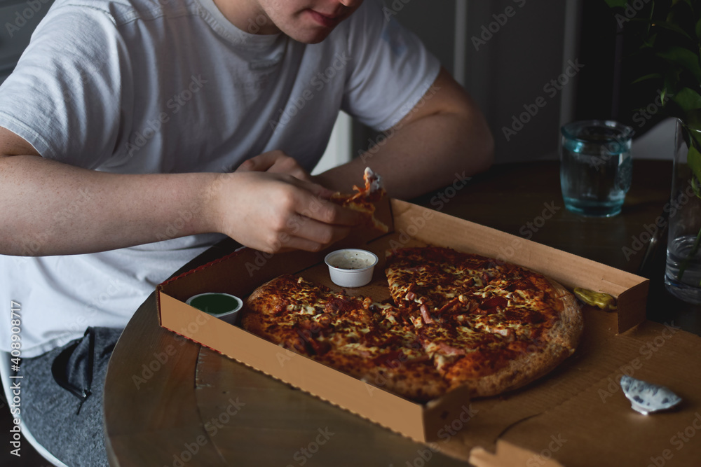 Young man eating pizza from cardboard box at home that was taken out or delivered home