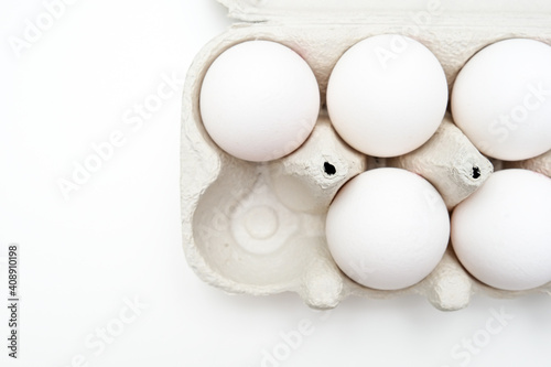 White eggs in recycled carton pressed box container on white table, one egg is taken out