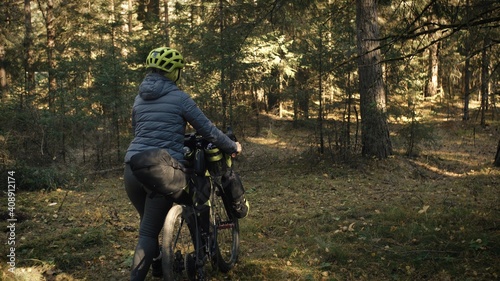 The woman travel on mixed terrain cycle touring with bike bikepacking outdoor. The traveler journey with bicycle bags. Stylish bikepacking, bike, sportswear in green black colors. Magic forest park.