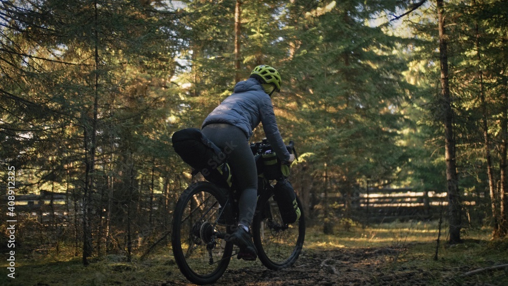 Naklejka premium The woman travel on mixed terrain cycle touring with bike bikepacking outdoor. The traveler journey with bicycle bags. Stylish bikepacking, bike, sportswear in green black colors. Magic forest park.