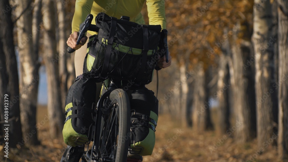 The woman travel on mixed terrain cycle touring with bikepacking. The traveler journey with bicycle bags. Sportswear in green black colors. The trip in magical autumn forest, arch, alley, avenue. The woman travel on mixed terrain cycle touring with bikepacking. The traveler journey with bicycle bags. Sportswear in green black colors. The trip in magical autumn forest, arch, alley, avenue.