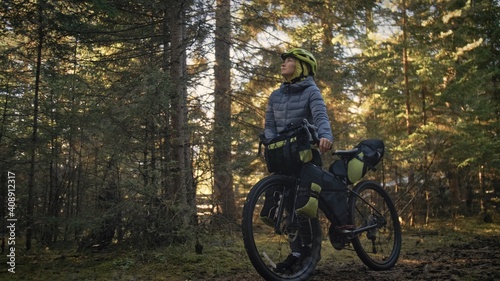 The woman travel on mixed terrain cycle touring with bike bikepacking outdoor. The traveler journey with bicycle bags. Stylish bikepacking, bike, sportswear in green black colors. Magic forest park.