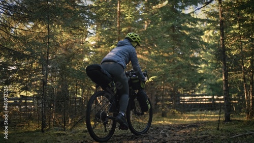 The woman travel on mixed terrain cycle touring with bike bikepacking outdoor. The traveler journey with bicycle bags. Stylish bikepacking, bike, sportswear in green black colors. Magic forest park. photo