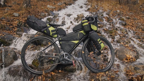 The mixed terrain cycle touring bike with bikepacking. The travel journey with light bicycle bags designed or modified for cycling. The trip on bike, outdoor in magical autumn forest, river stream.