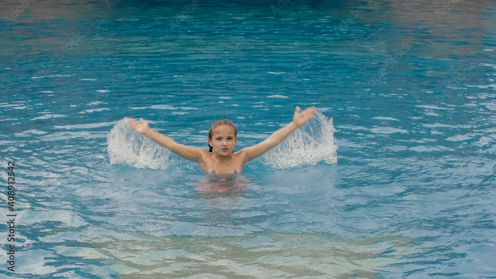 The little cute girl have fun in the swim pool. The child enjoy summer vacation in a swimming pool jumping, spinning, splash water. Slow motion. Happy childhood.