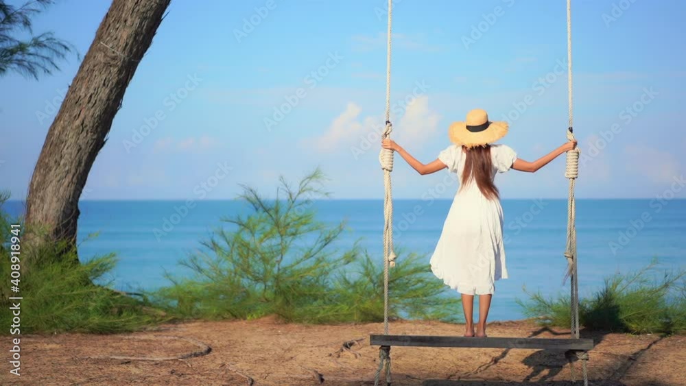 Back view of girl standing on swing in front of sea. Slow-motion