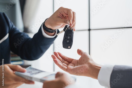 Closeup hand giving a car key and money for loan credit financial, lease and rental concept